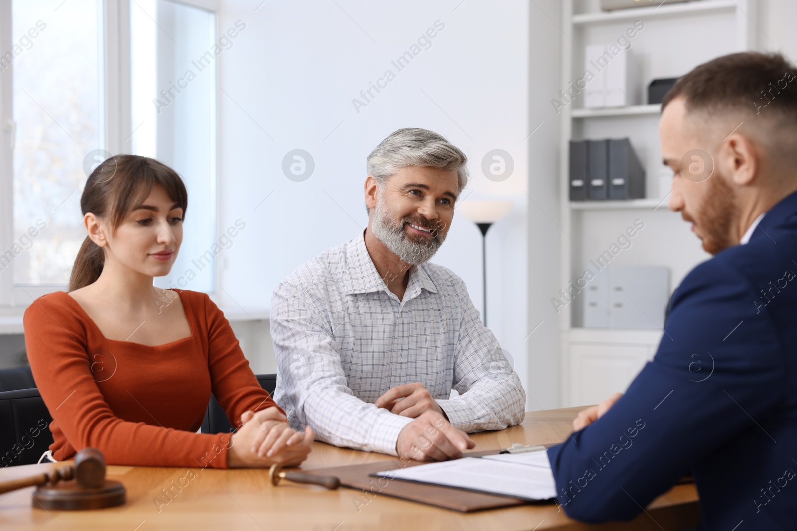 Photo of Couple having meeting with professional notary at wooden desk indoors