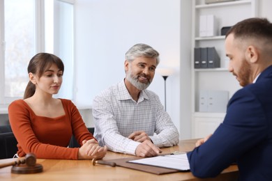 Photo of Couple having meeting with professional notary at wooden desk indoors