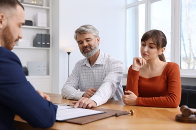 Photo of Couple having meeting with professional notary at wooden desk indoors