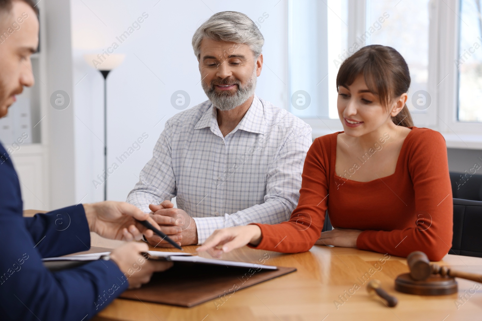 Photo of Couple having meeting with professional notary at wooden desk indoors