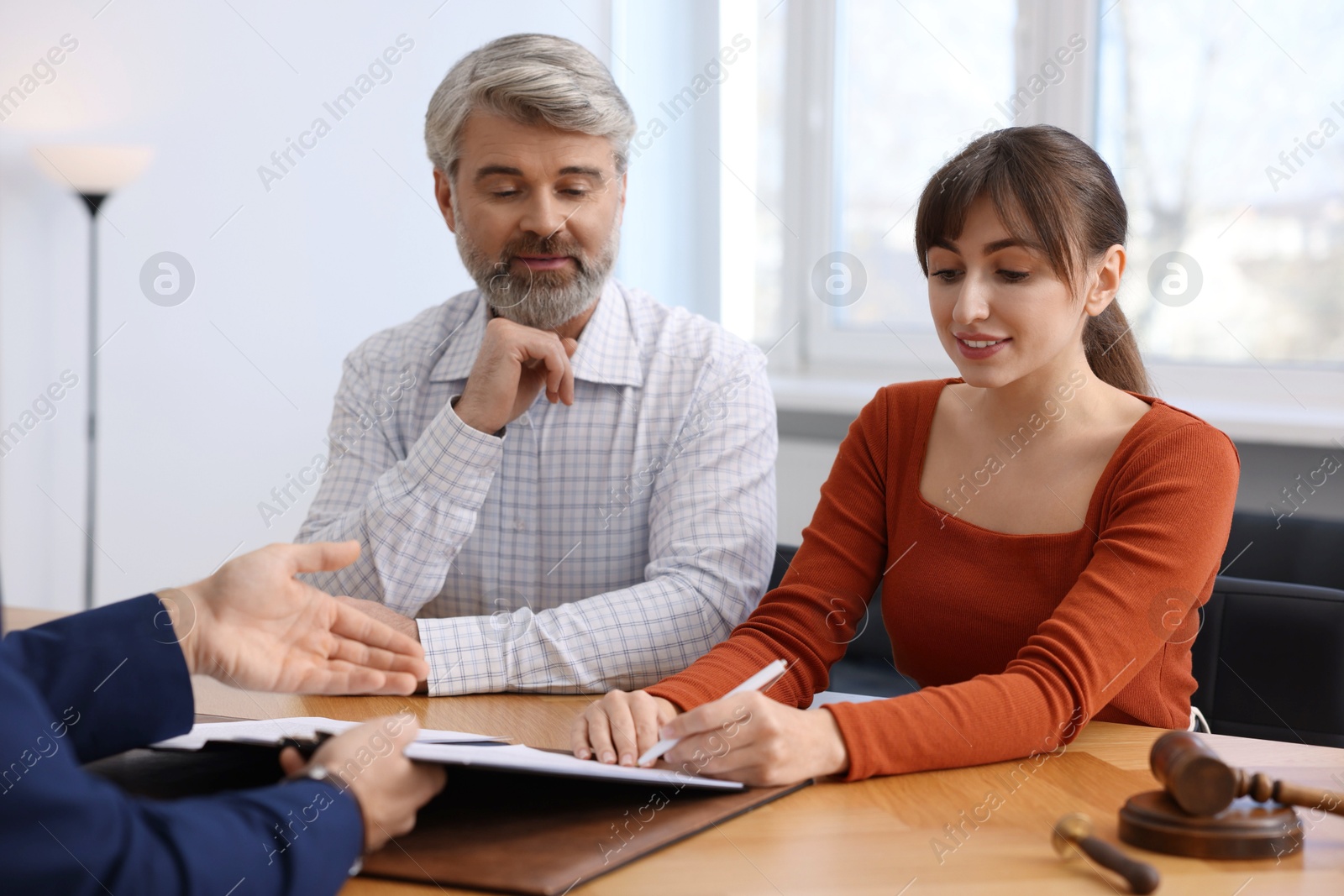 Photo of Clients signing notarial paperwork during meeting with lawyer at wooden desk indoors