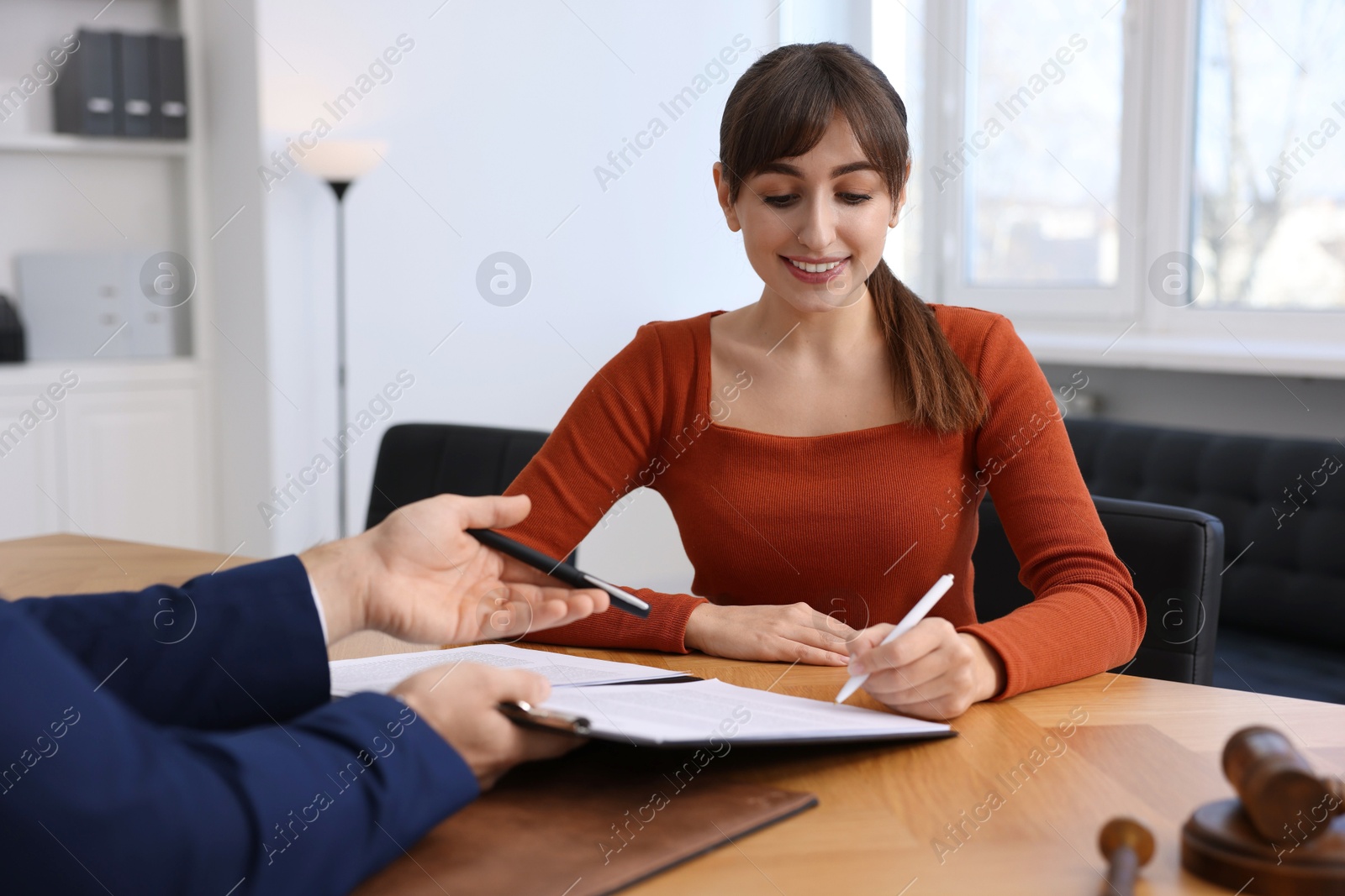 Photo of Client signing notarial paperwork during meeting with lawyer at wooden desk indoors