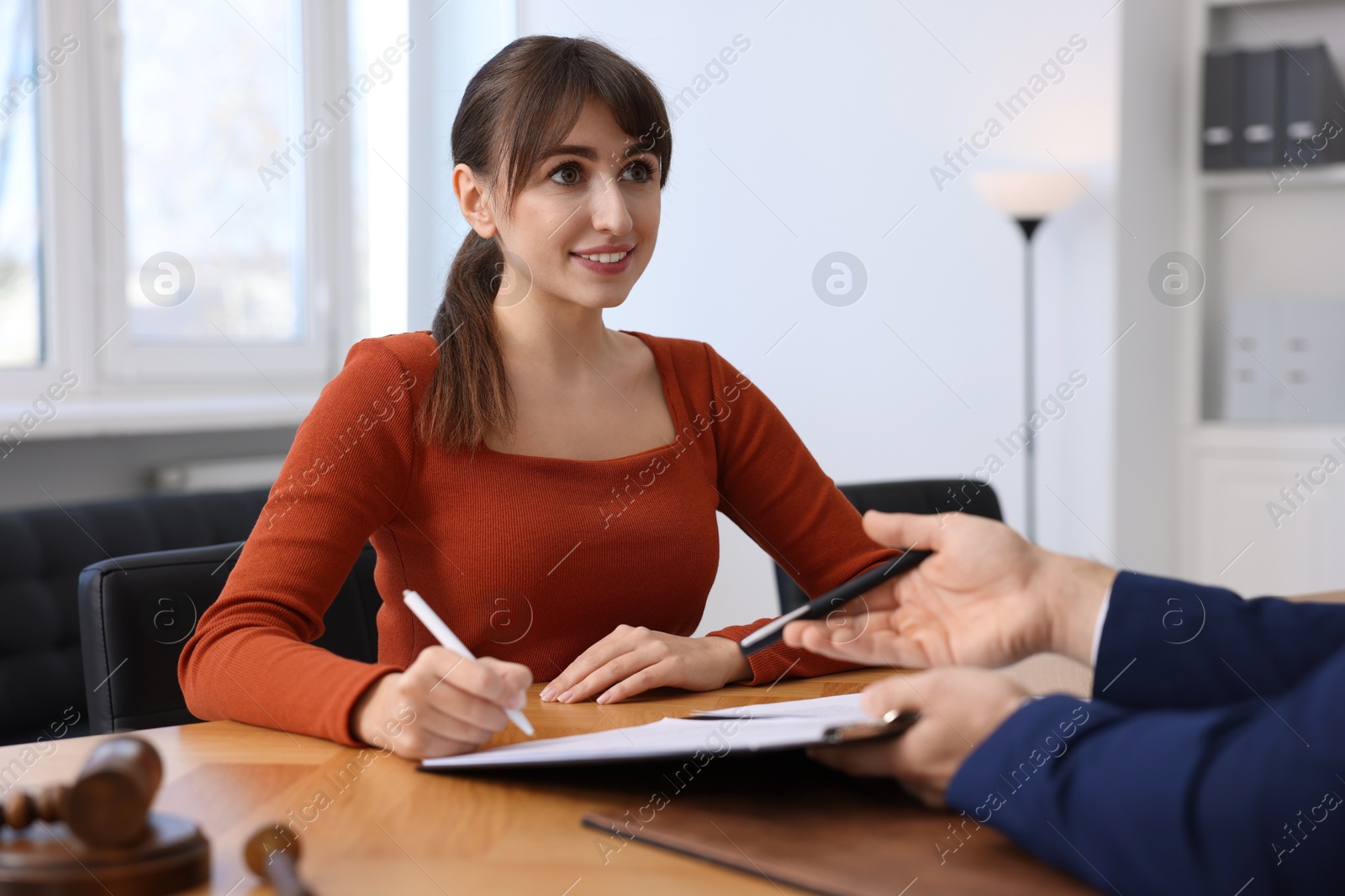 Photo of Client signing notarial paperwork during meeting with lawyer at wooden desk indoors