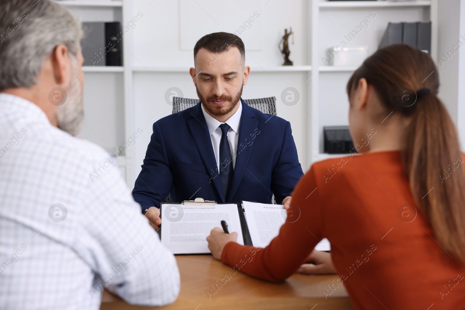 Photo of Clients signing notarial paperwork during meeting with lawyer at wooden desk indoors