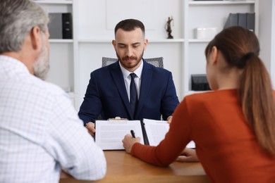 Clients signing notarial paperwork during meeting with lawyer at wooden desk indoors