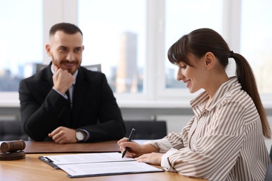 Photo of Client signing notarial paperwork during meeting with lawyer at wooden desk indoors, selective focus