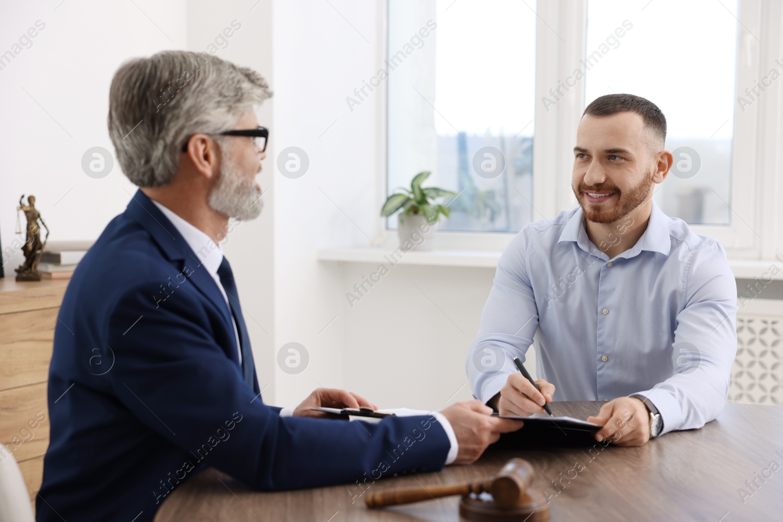 Photo of Client signing notarial paperwork during meeting with lawyer at wooden desk indoors, selective focus