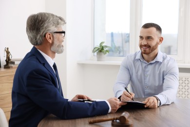 Client signing notarial paperwork during meeting with lawyer at wooden desk indoors, selective focus