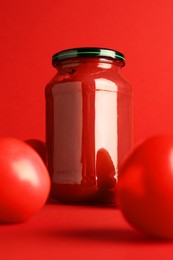 Photo of Ketchup in glass jar and fresh tomatoes on red background