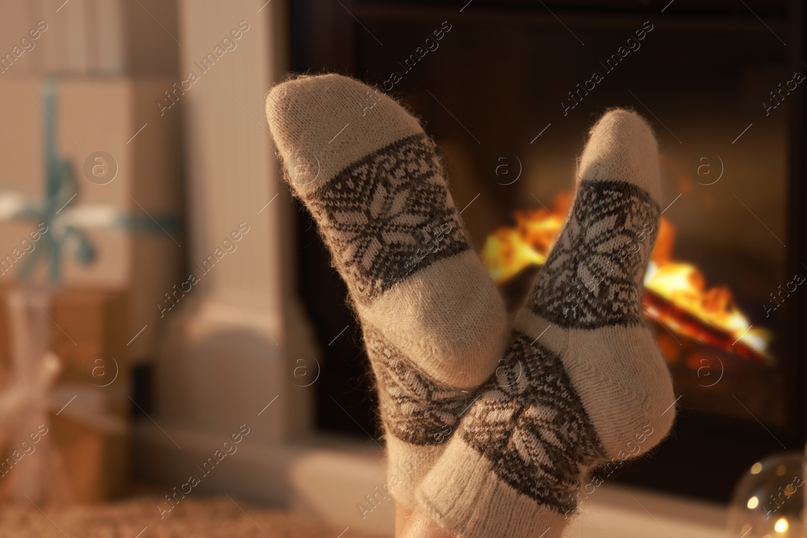 Photo of Woman in warm socks resting near fireplace at home, closeup