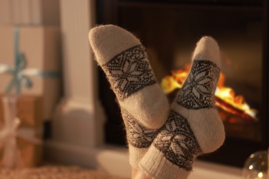 Photo of Woman in warm socks resting near fireplace at home, closeup