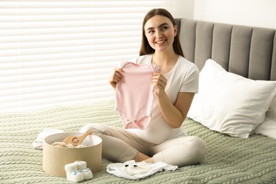 Photo of Pregnant woman with baby clothes on bed at home