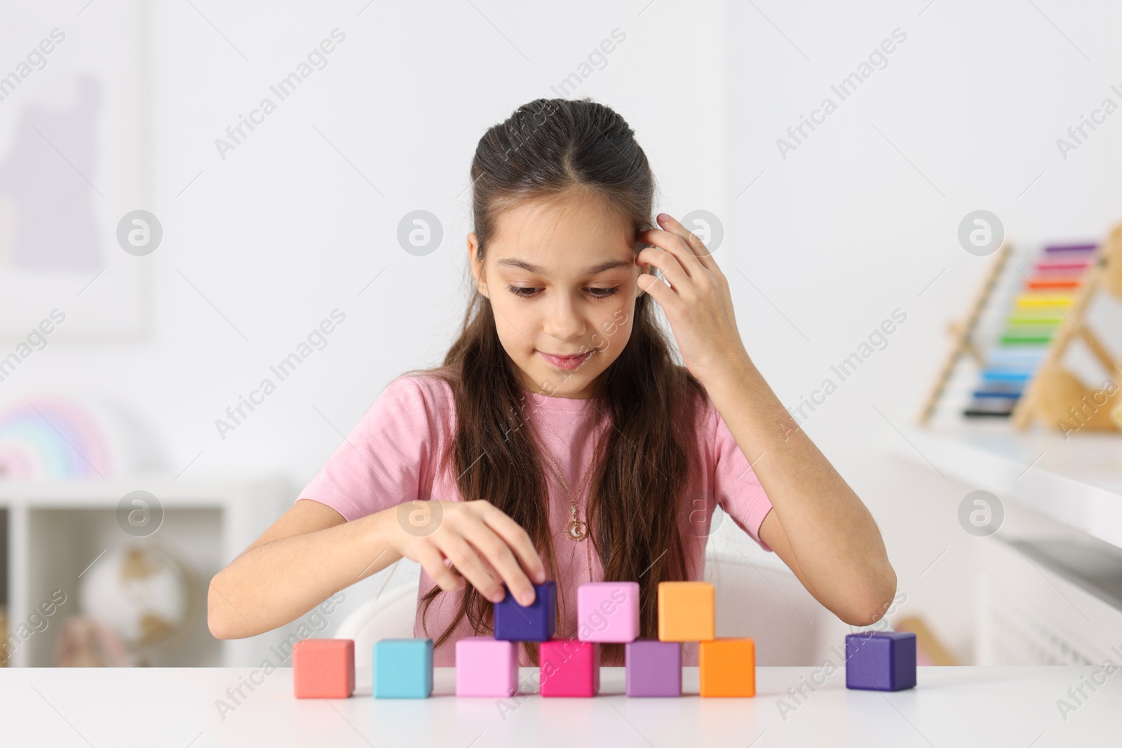 Photo of Happy girl building pyramid of colorful cubes at table indoors