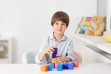 Photo of Boy building tower of colorful cubes at table indoors