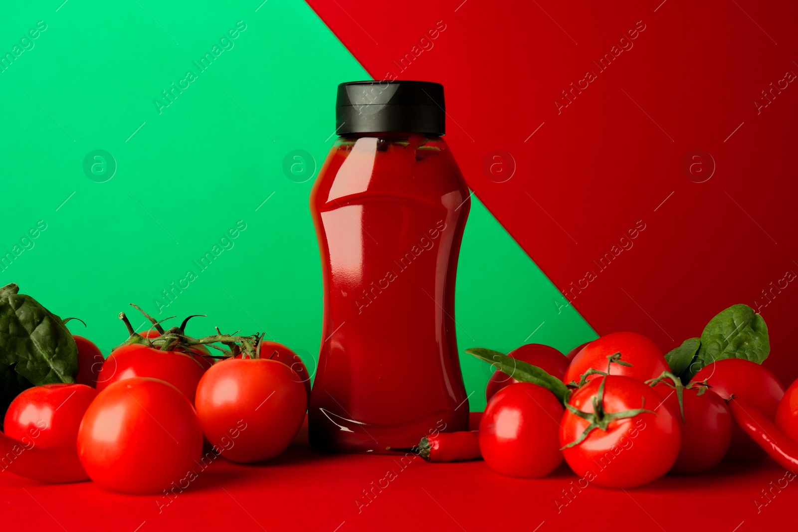 Photo of Ketchup, tomatoes, chili peppers and spinach on color background