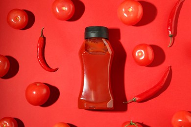 Photo of Bottle of ketchup, tomatoes and chili peppers on red background, flat lay