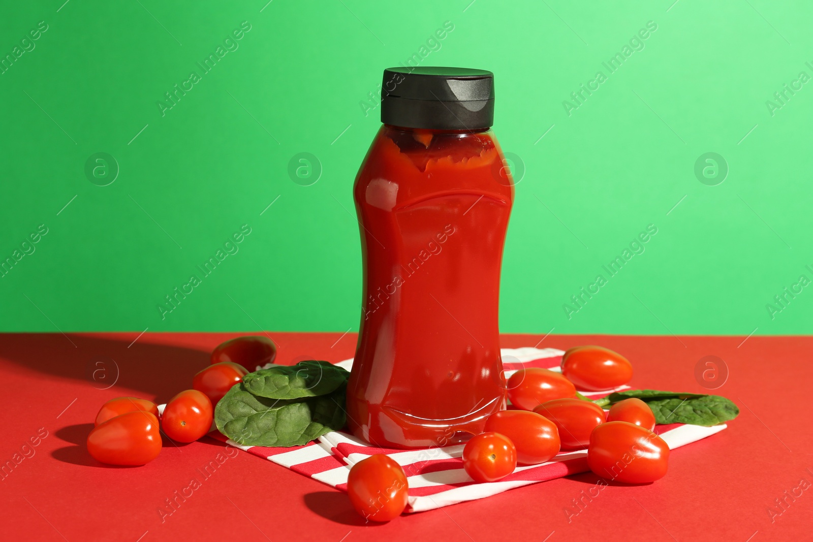 Photo of Ketchup, tomatoes and spinach on color background