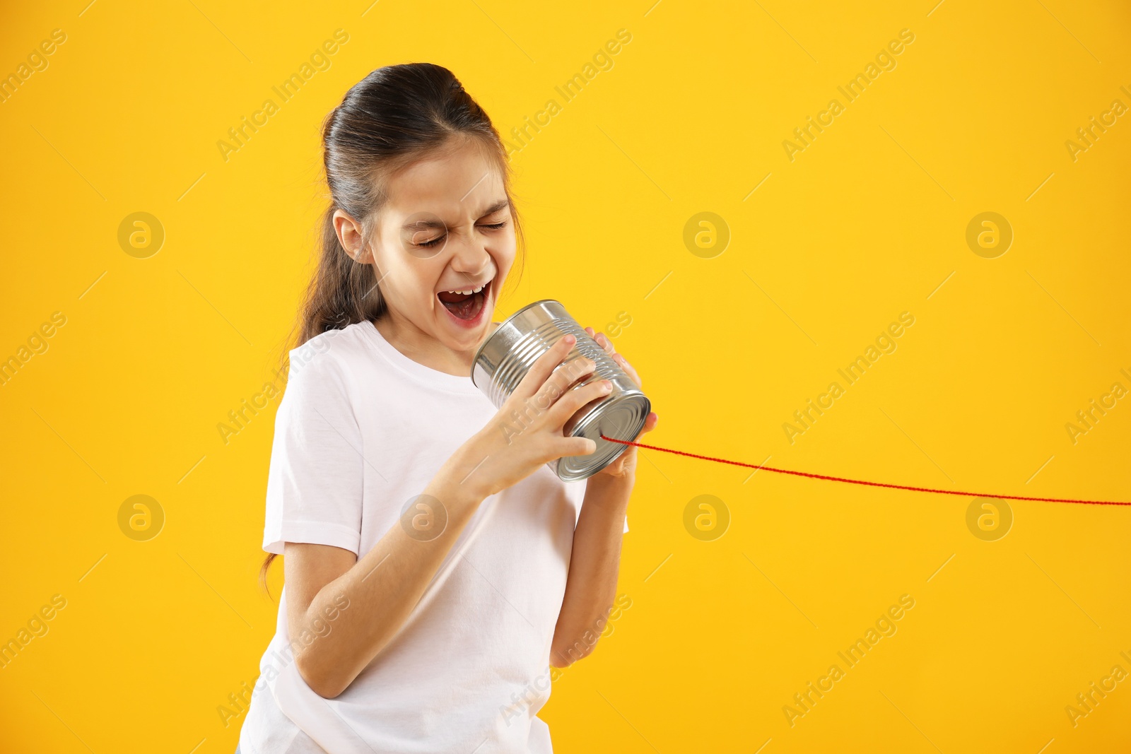 Photo of Girl using tin can telephone on yellow background