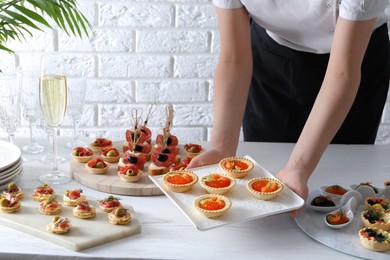 Photo of Woman with many different tasty canapes at white wooden table, closeup