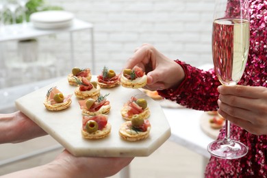 Photo of Woman taking tasty canape from waiter with board indoors, closeup