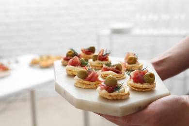 Photo of Woman holding board with tasty canapes indoors, closeup