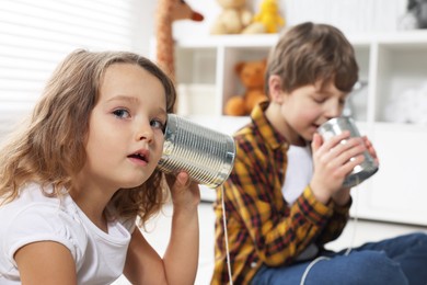 Photo of Boy and girl talking on tin can telephone indoors, selective focus