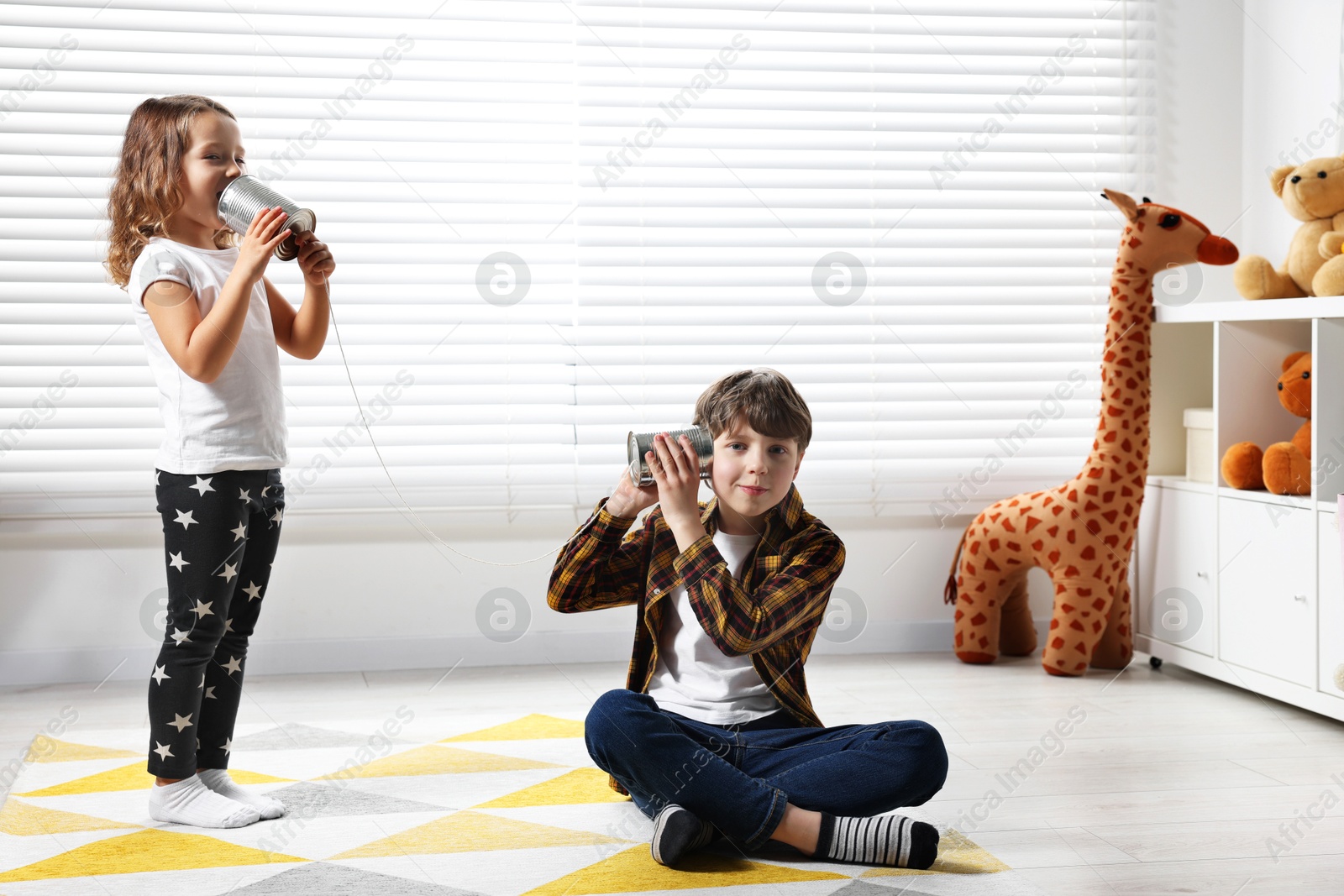 Photo of Boy and girl talking on tin can telephone indoors