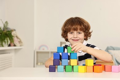 Photo of Little boy stacking colorful cubes at white table indoors, space for text