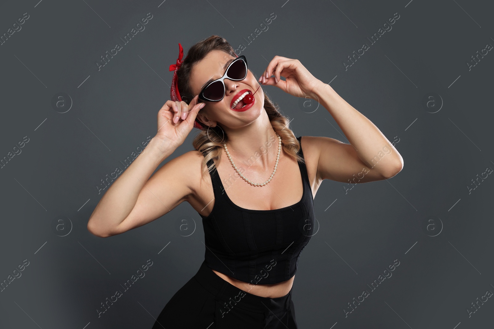 Photo of Beautiful woman eating cherry on grey background. Pin-up vibes