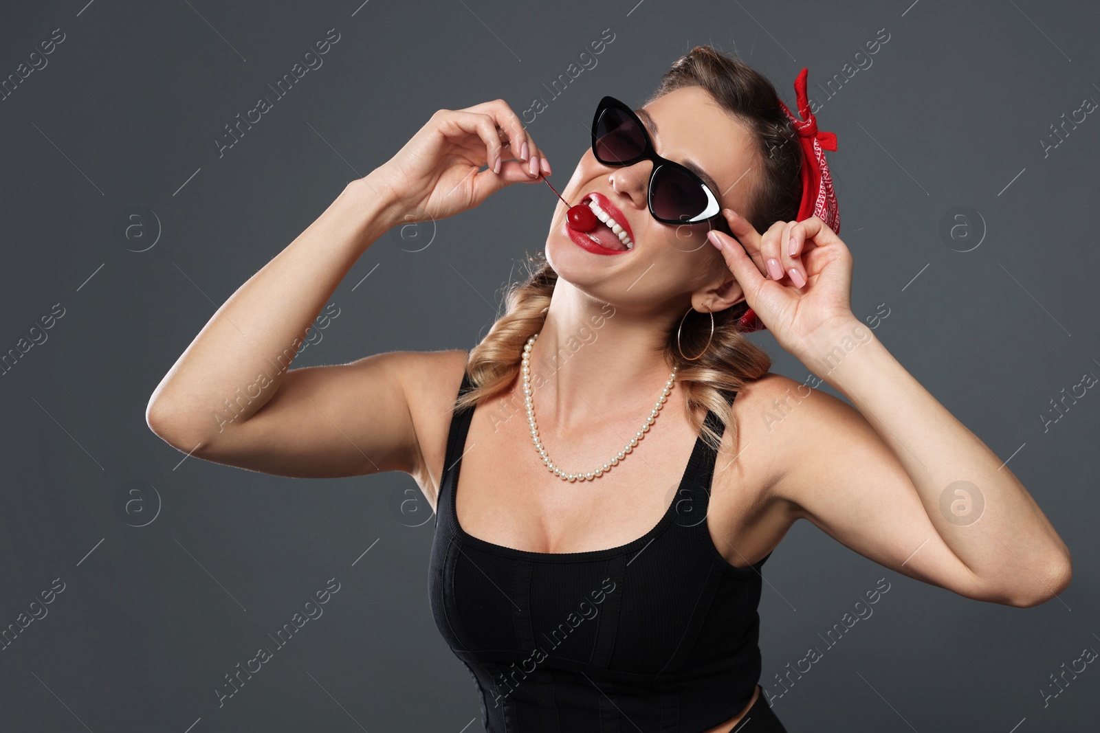 Photo of Beautiful woman eating cherry on grey background. Pin-up vibes