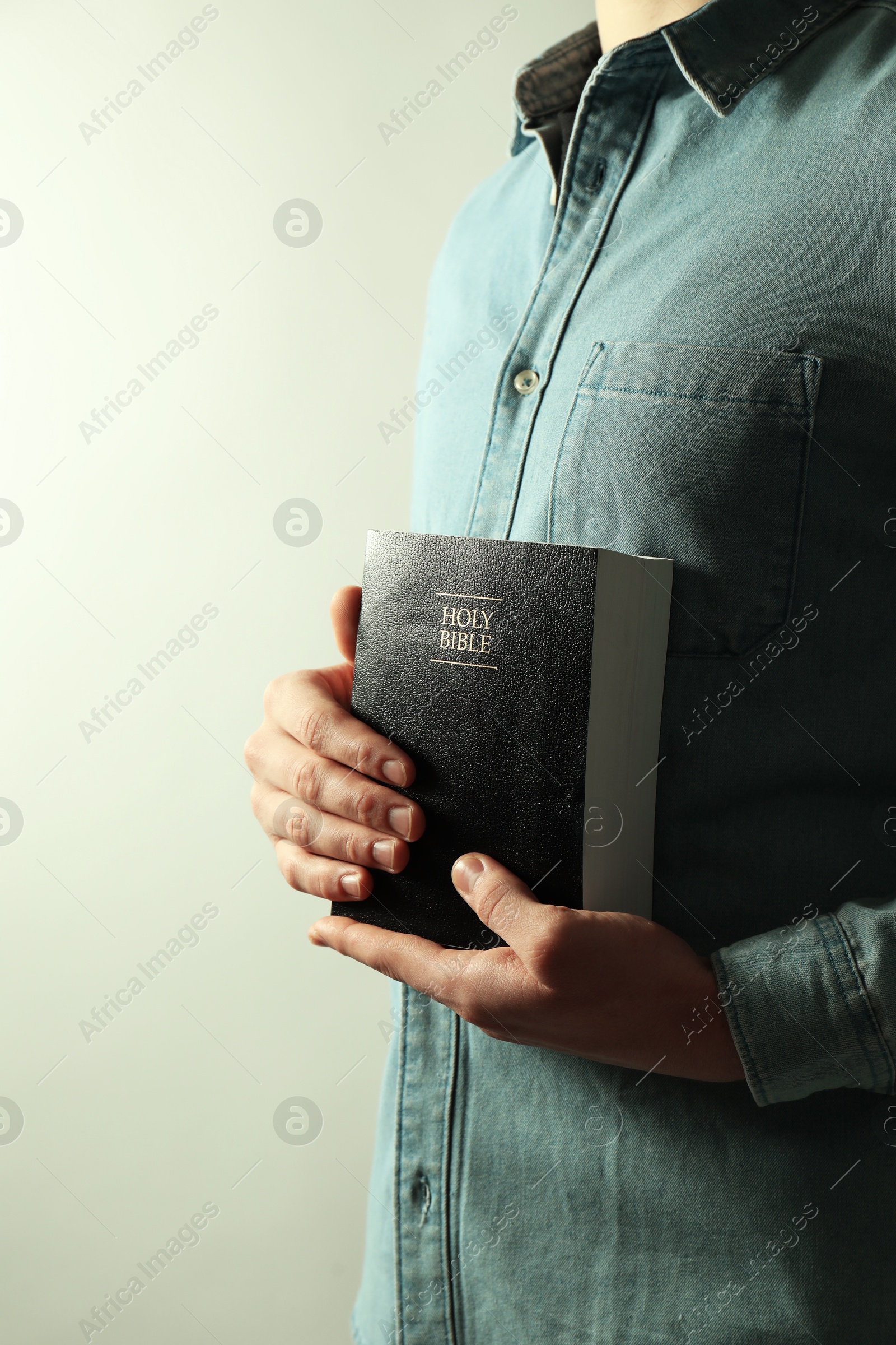 Photo of Man with hardcover Holy Bible on light background, closeup. Space for text