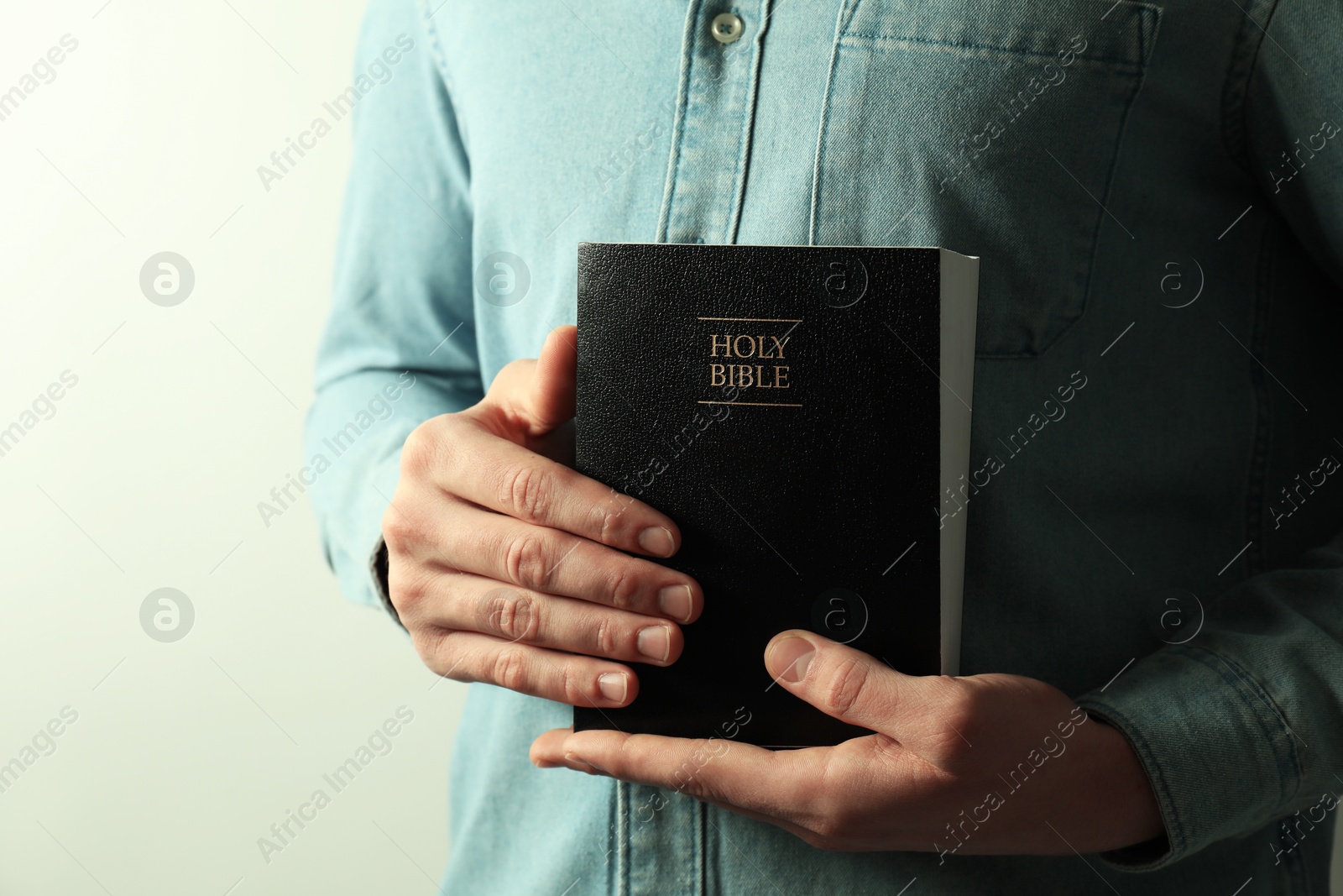 Photo of Man with hardcover Holy Bible on light background, closeup. Space for text