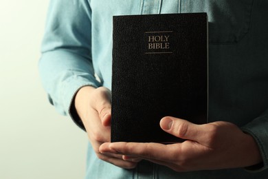 Photo of Man with hardcover Holy Bible on light background, closeup