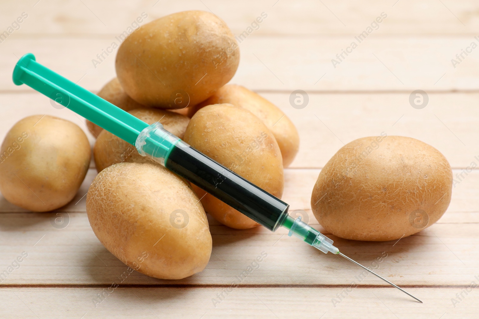 Photo of GMO concept. Potatoes and syringe on wooden table, closeup