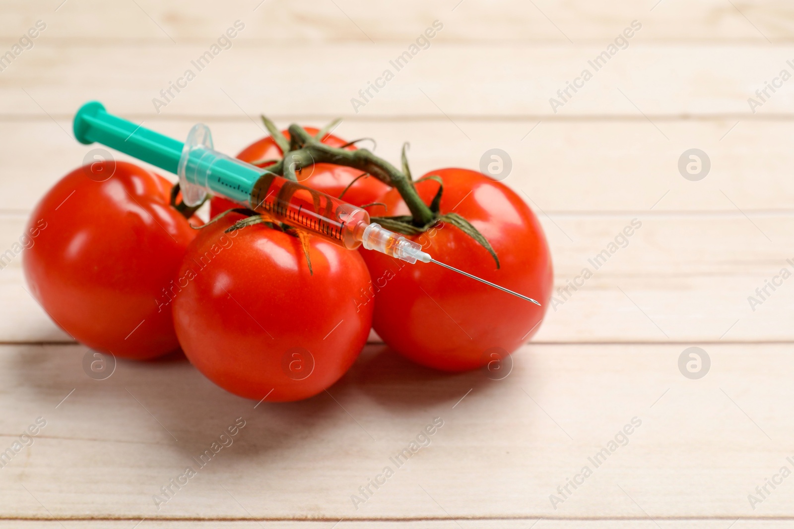 Photo of GMO concept. Fresh tomatoes and syringe on wooden table, closeup. Space for text