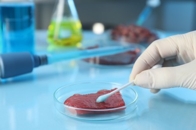 Photo of GMO concept. Scientist with swab and piece of meat at table in laboratory, closeup. Space for text