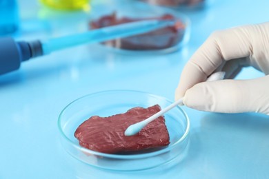 Photo of GMO concept. Scientist with swab and piece of meat at table in laboratory, closeup. Space for text