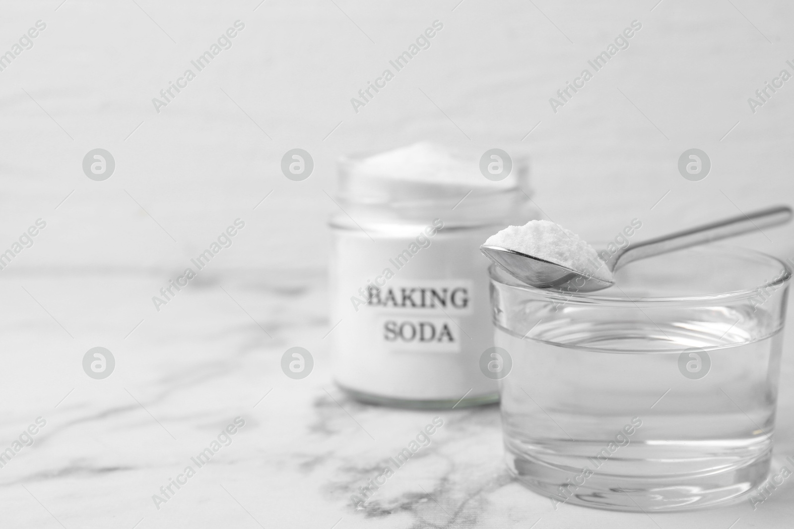 Photo of Glass of water and baking soda on white marble table, selective focus. Space for text