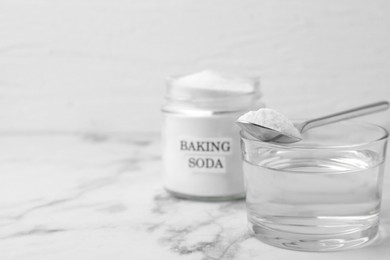 Photo of Glass of water and baking soda on white marble table, selective focus. Space for text