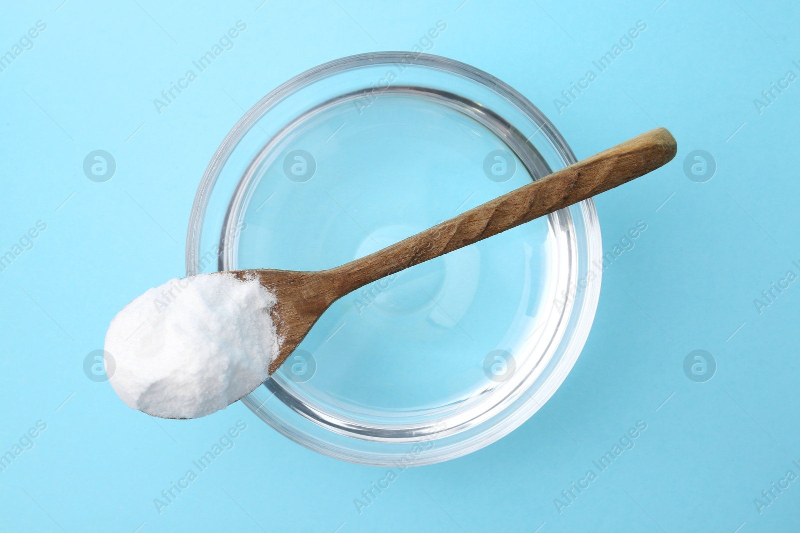 Photo of Glass of water and baking soda on light blue background, top view