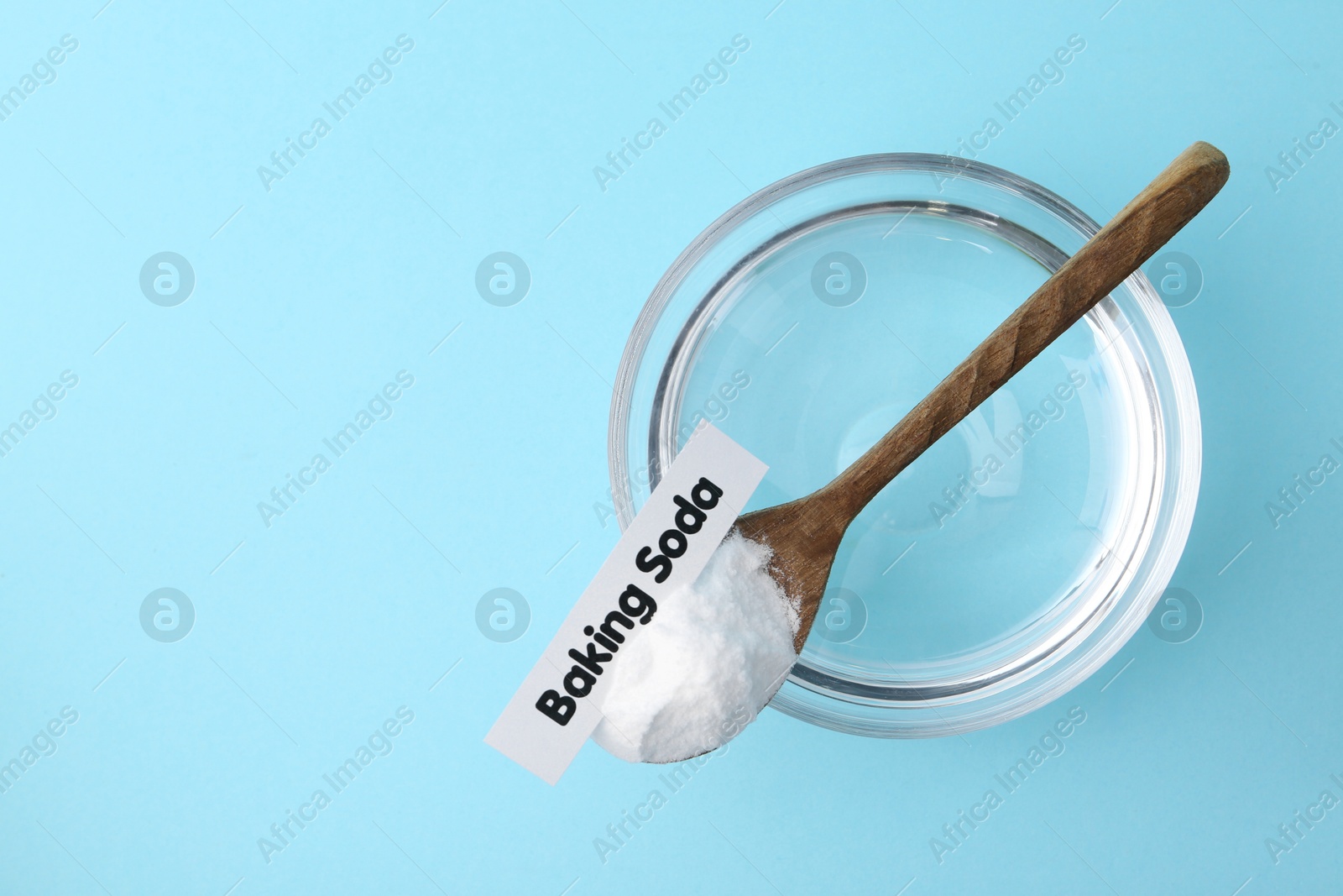 Photo of Glass of water and baking soda on light blue background, top view. Space for text