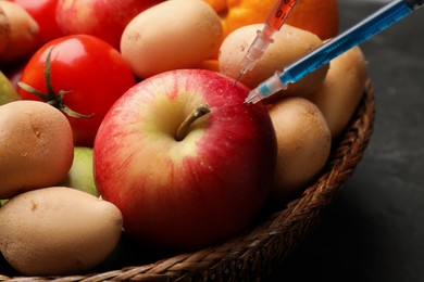 Photo of GMO concept. Red apple with different syringes in basket on grey table, closeup