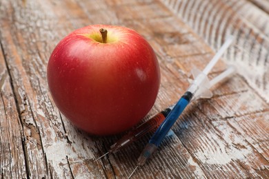 Photo of GMO concept. Red apple and syringes on rustic wooden table, closeup