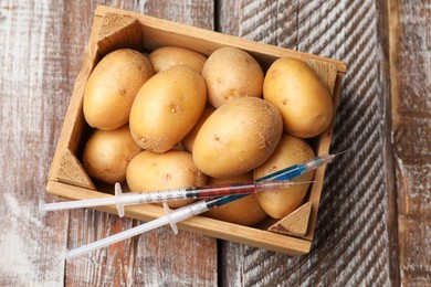 Photo of GMO concept. Potatoes in crate and syringes with liquid on rustic wooden table, top view