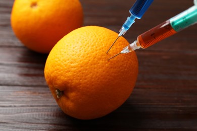 Photo of GMO concept. Orange with syringes on wooden table, closeup