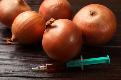 Photo of GMO concept. Onion bulbs and syringe on wooden table, closeup