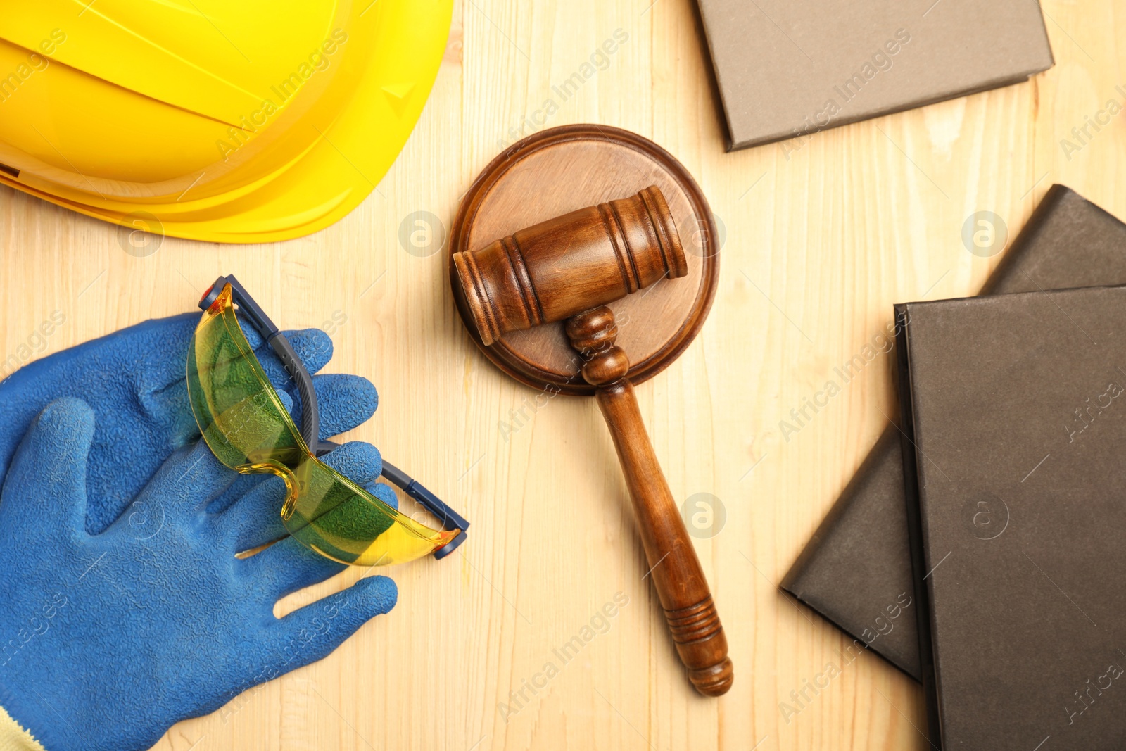 Photo of Accident at work concept. Gavel, books and protective gear on wooden table, flat lay