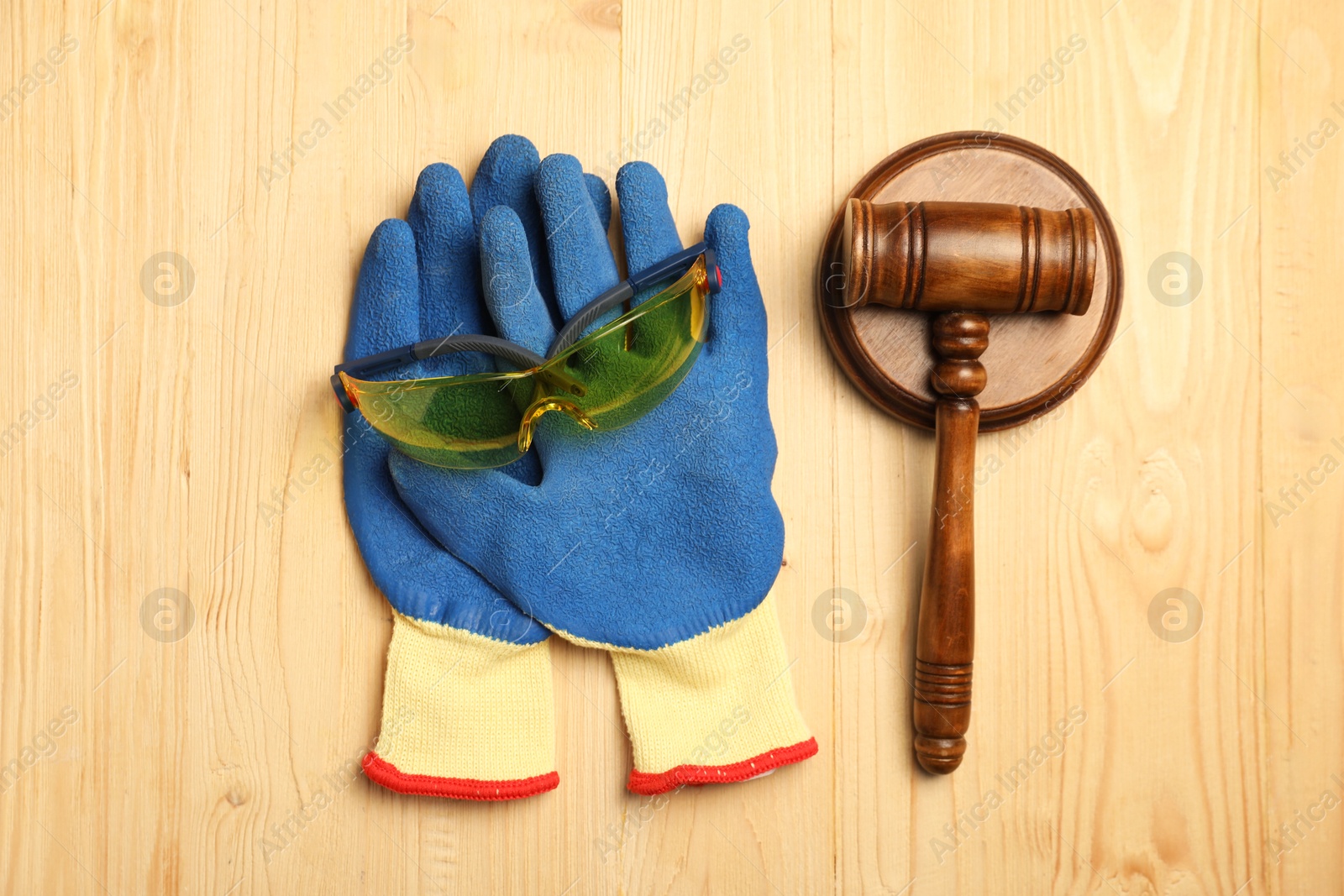 Photo of Accident at work concept. Gavel, protective gloves and goggles on wooden table, flat lay