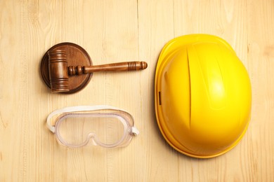 Photo of Accident at work concept. Gavel, hardhat and protective goggles on wooden table, flat lay