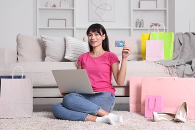 Internet shopping. Happy woman with credit card, laptop and colorful bags at home